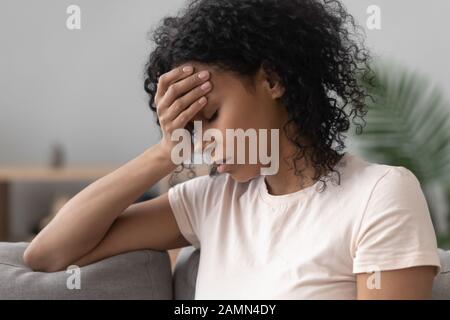 African woman sitting on couch feels unhappy having problems Stock Photo