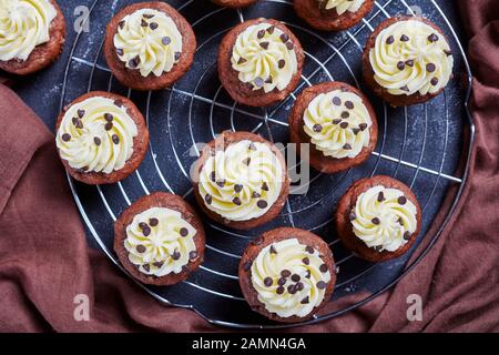 Chocolate pecan cupcakes topped with buttercream swirl icing on a metal cake rack on a concrete table, horizontal view from above, flat lay, macro Stock Photo
