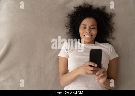Top view beautiful african woman holding smartphone lying in bed Stock Photo