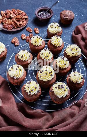 Chocolate pecan cupcakes topped with buttercream swirl icing on a metal cake rack on a concrete table, vertical view from above Stock Photo