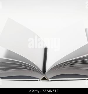 Mockup of closed blank square book and black pencil at white textured paper background Stock Photo
