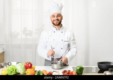 Chef Man Using Whisk Mixing Ingredients In Saucepan In Kitchen Stock Photo