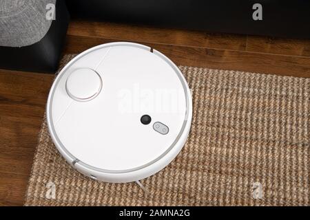 Robotic vacuum cleaner runs under sofa in room on laminate floor modern smart cleaning technology housekeeping. Stock Photo