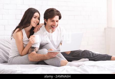 Excited spouses enjoying information on laptop, resting in bed Stock Photo