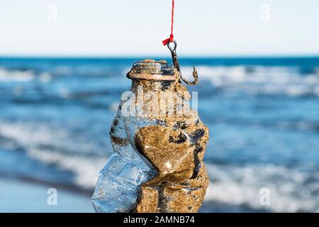 closeup of a used plastic bottle, covered with wet sand, in a fish hook, freshly fished in the ocean Stock Photo