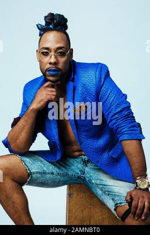 Portrait of a man with blue lips dressing in blue sitting . Studio photo shoot. Pride. Stock Photo