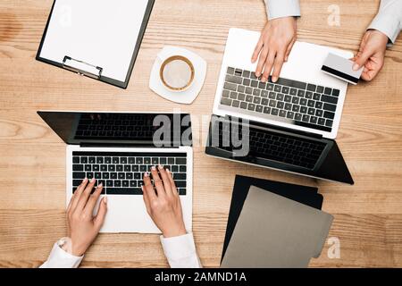 Top view of colleagues using laptops with credit card on table, cropped view Stock Photo
