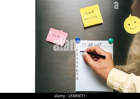 cropped view of man filling in to do list hanging on fridge near wishes on sticky notes isolated on white Stock Photo