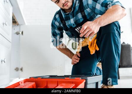 cropped view of handyman looking at tools near opened toolbox in kitchen Stock Photo