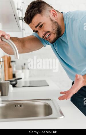 stressed man touching faucet and gesturing in kitchen Stock Photo