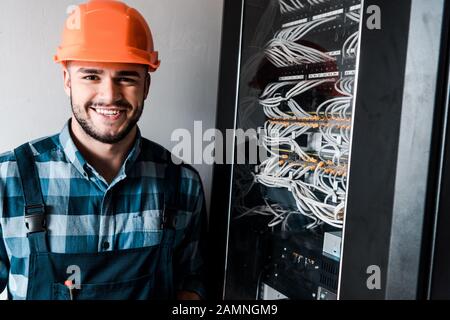 happy technician looking at camera near wires and cables Stock Photo