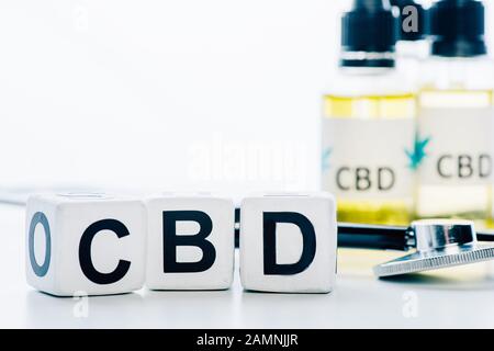 selective focus of cannabis oil in bottles with lettering cbd, cubes and stethoscope on white background Stock Photo
