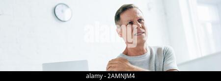 panoramic shot of handsome man feeling pain in shoulder in apartment Stock Photo