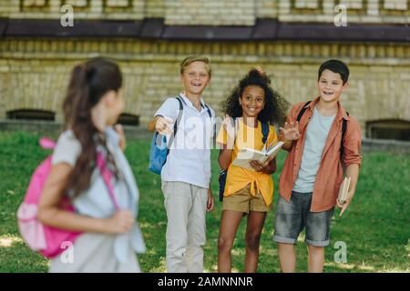 selective focus of multicultural schoolkids waving hands to schoolgirl Stock Photo