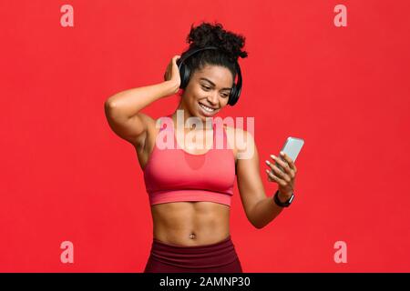 Happy black fitness girl choosing music on smartphone for exercising Stock Photo