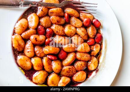 Closeup flat top view above of vibrant red wine sauce potato gluten free wheat gnocchi on white plate with lupine beans marinated in Italian Italy res Stock Photo