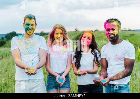 happy multicultural friends holding colorful holi paints in hands Stock Photo