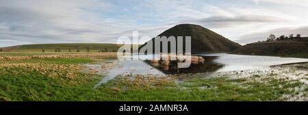 The huge Neolithic chalk mound of Silbury Hill, Avebury, Wiltshire, UK, reflected in a flooded meadow. It is 40m high and was built around 2300 BC Stock Photo