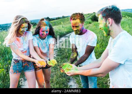 happy multicultural friends holding colorful holi paints in hands Stock Photo