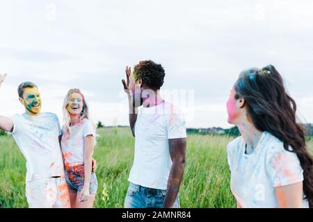 selective focus of multicultural friends with holi paints on faces waving hands Stock Photo