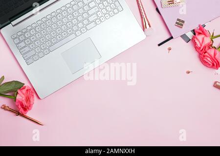 Feminine desk workspace concept. Top view of laptop, golden color stationery and roses on pink table. Stock Photo