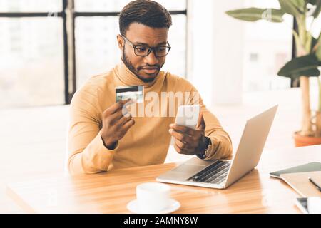 Black manager making purchases using computer and phone Stock Photo
