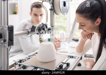 Engineering students using an innovative 3D printer in the university lab, they are printing a prototype together, creativity and education concept Stock Photo