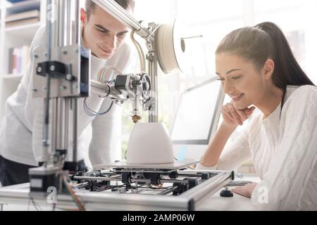 Engineering students using an innovative 3D printer in the university lab, they are printing a prototype together, creativity and education concept Stock Photo