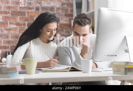 Young academic students at the library, they are studying together and reading a book Stock Photo