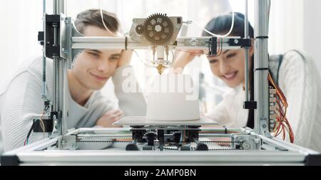 Engineering students using an innovative 3D printer in the university lab, they are printing a prototype together, creativity and education concept Stock Photo