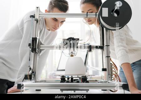 Engineering students using an innovative 3D printer in the university lab, they are printing a prototype together, creativity and education concept Stock Photo