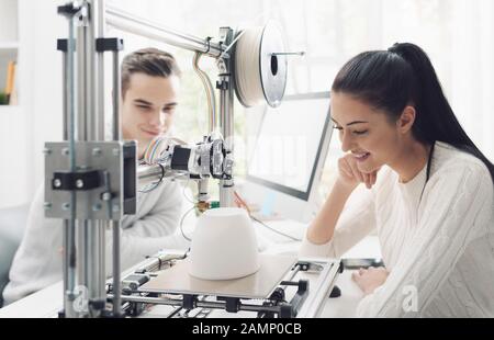Engineering students using an innovative 3D printer in the university lab, they are printing a prototype together, creativity and education concept Stock Photo