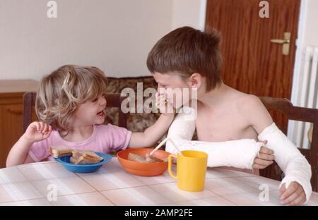 accident prone boy with two broken arms in plaster being fed by his little sister Stock Photo