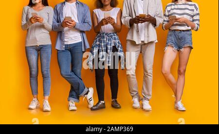 Cropped of multiethnic friends uisng smartphones over yellow background Stock Photo