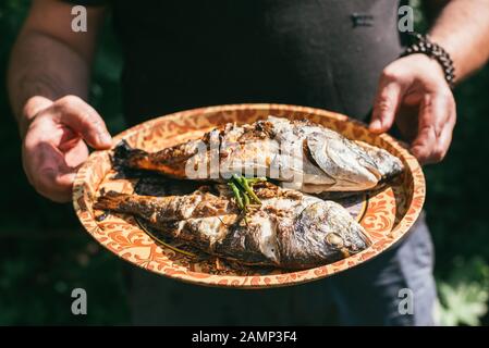 A man holds a plate with a ready meal. delicious and fresh grilled fish with lemon on the Barbeque grill at the garden in summer. Selective focus macr Stock Photo