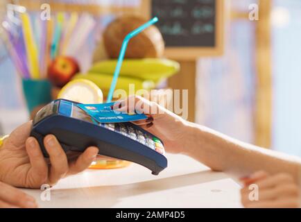 Woman at the bar paying using a contactless credit card, she is leaning it on the POS teminal, payments and technology concept Stock Photo