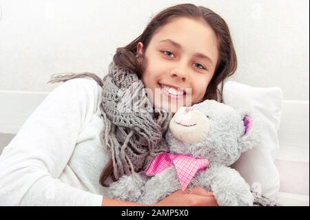 Teen girl is sick in bed with a toy teddy bear Stock Photo