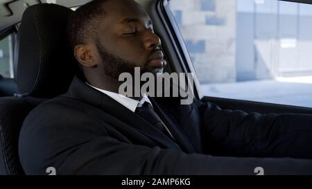 Exhausted of active way of life black man falling asleep in car, tired of work Stock Photo