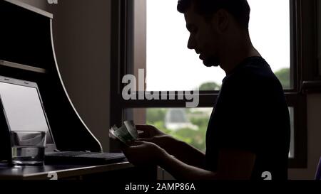 Successful young man counting money, silhouette of student planning budget Stock Photo