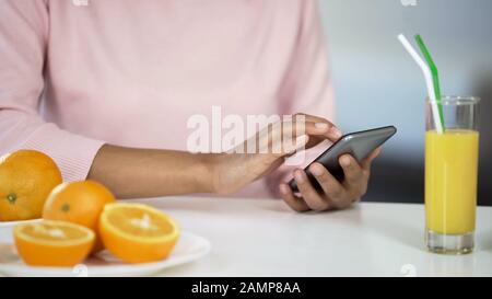 Multiracial girl using smartphone in kitchen, oranges on table, healthcare food Stock Photo