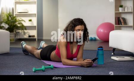 Fit young lady setting application on phone, lying mat, checking workout results Stock Photo