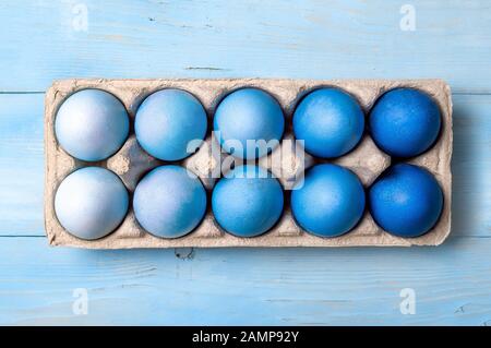 Easter concept. Ombre eggs in blue colors in cardboard packaging on blue wooden background. Top down view or flat lay. Classic blue colors in Easter 2020 Stock Photo