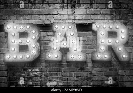 Bar signboard. Inscription from large metal letters decorated with glowing light bulbs on the brick wall Stock Photo