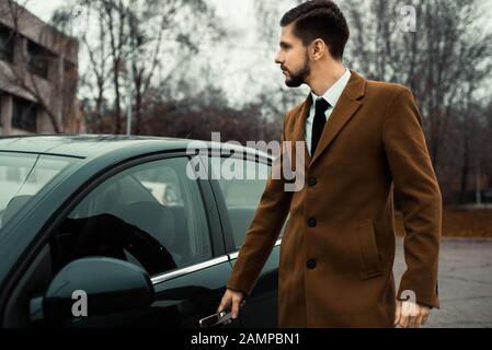 Portrait of a young bearded guy thirty years old. A businessman in a business suit, with a tie, stands against the backdrop of a car. Business concept Stock Photo