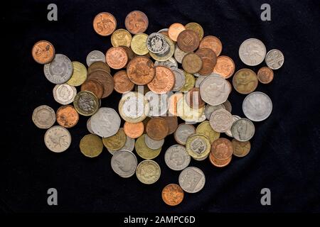 A pile of various types of coins of different shapes, sizes and of different compositions from various countries on a black background