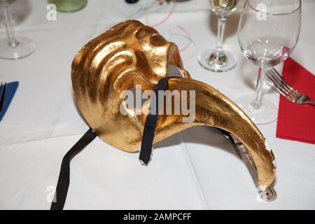 A golden masquerade ball mask on a dinner table. Venetian Eye Mask carnival, Fancy Dress Accessory, Carnival Party Costume Ball. Stock Photo