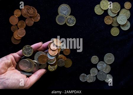 Piles of various types of coins of different shapes sizes and from various countries organized by metal type on a black background
