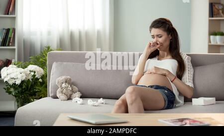 Upset pregnant lady crying on sofa, hormonal disorder emotional problems Stock Photo