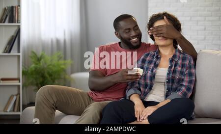 Happy black man making surprise to girlfriend, holding gift box in hand, care Stock Photo