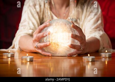 Fortune Teller with Crystal Ball on table with candles and black and red mottled background Stock Photo